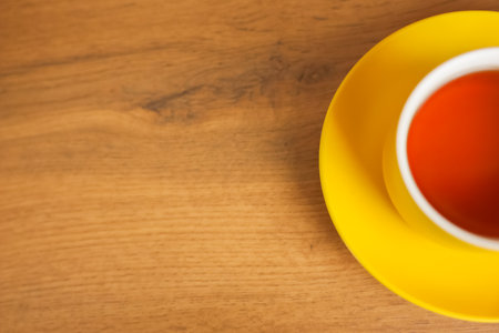 A yellow cup and saucer stands on a wooden background with black tea poured, half of a mug with space for text is visible. The concept of tea drinking, tea tradition, break. High quality photoの写真素材