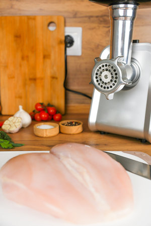 Chicken fillet lies on a white cutting board against the background of a meat grinder, vegetables and spices. The concept of dietary recipes, proper and healthy nutrition, the cooking process. High quality photoの写真素材