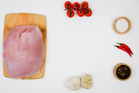 On the left is a piece of turkey fillet lying on a wooden cutting board on a white background, with seasoning in wooden bowls on the edges, herbs and vegetables forming a place for the text in the center. The concept of healthy eating, dietary and natural products, cooking. High quality photoの写真素材
