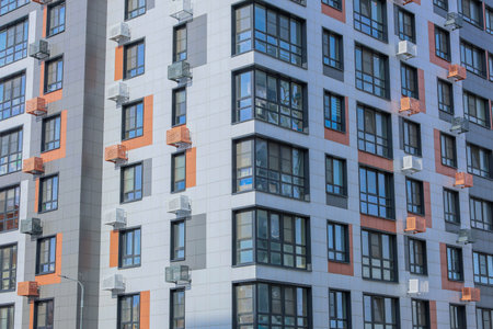 The concept of modern architecture, a residential complex, an apartment building for living. Close-up of the corner of the house in the camera multi-storey, apartment building in gray and white tones with orange inserts of modern architecture with large windows and framed balconies and baskets for air conditioning. High quality photoの写真素材