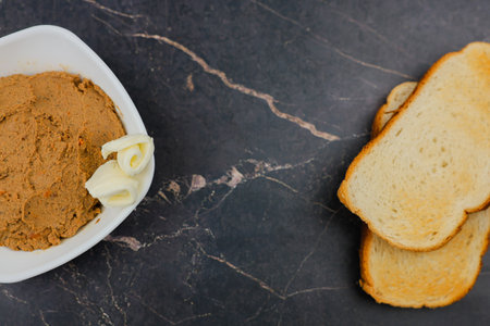 A white plate with liver pate and slices of butter stands on the left on a dark background, on the right there are wheat bread toasts with space for text in the center. The concept of snacking, wholesome and healthy food. High quality photoの写真素材