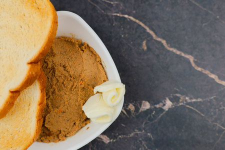 Close-up of a white plate with liver pate and slices of butter, wheat bread toast on top on a dark...