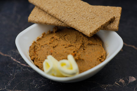 Close-up of a white plate with liver pate and slices of butter, bread on top of it on a dark...