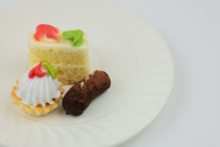 Small cakes of different flavors and sizes lie on a white plate on a white background. The concept...