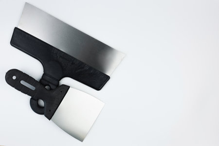 Metal spatulas with black handles lie on the side on a white background with space for text. The concept of repair, construction. High quality photoの写真素材