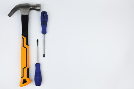 A hammer with an iron base and a yellow-black handle lies on the left, next to it are screwdrivers on a white background with space for text. The concept of repair, hammering. High quality photoの写真素材