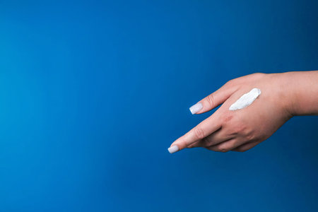 A close-up hand on the right on a blue phonet, with a white textured stroke of cream with space for...