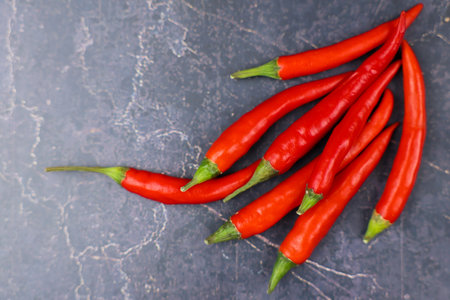 Bright red chilies arranged on a textured dark surface, perfect for cooking or spice-related themes.