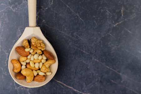 A beautifully crafted wooden spoon is filled with a colorful variety of nuts placed on a dark textured surfaceの写真素材