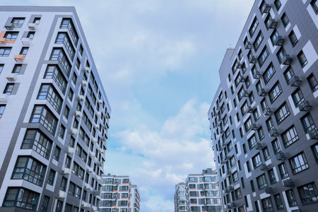 Contemporary apartment buildings beautifully framed by a serene sky that features soft, fluffy clouds above themの写真素材