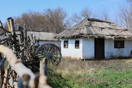 A charming countryside house featuring a thatched roof beautifully situated amongst lush greenery and a rustic fenceの写真素材
