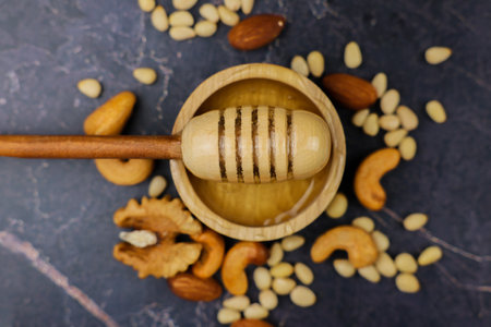 Close-up in the center, liquid yellow honey in a wooden bowl with a wooden spoon stands on a dark background surrounded by a mix of nuts. The concept of healthy snacks, proper nutrition. High quality photoの写真素材