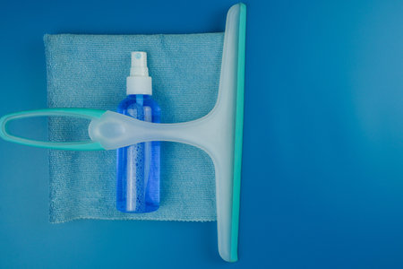 A squeegee along with a blue spray bottle is conveniently placed on a soft towel for effective...