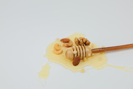 Close-up in the center of a mix of nuts lies in a puddle of liquid yellow honey, in the center lies a wooden spoon on a white background in close-up. The concept of a healthy snack, a natural dessert, sweet. High quality photoの写真素材