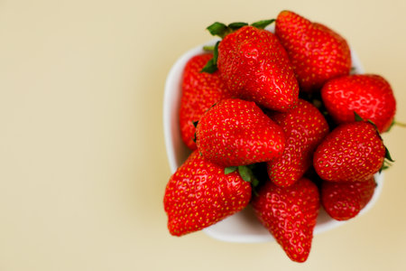 A white plate of strawberries stands on the side on a beige background with space for text. Concept...