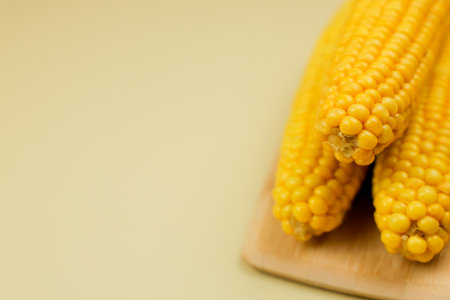 Yellow ripe peeled corn cobs with large grains lie on a wooden board on the side on a yellow...