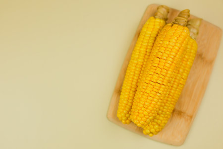 Top view of yellow ripe peeled ears of corn with large grains lying on a wooden board on the side on a yellow background with space for text. The concept of healthy nutrition, natural iron, corn cultivation. High quality photoの写真素材