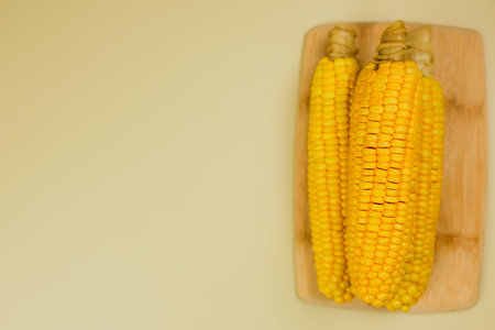 Top view of yellow ripe peeled ears of corn with large grains lying on a wooden board on the side on a yellow background with space for text. The concept of healthy nutrition, natural iron, corn cultivation. High quality photoの写真素材