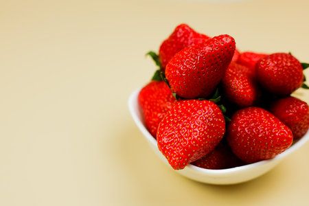 Side view of ripe strawberries in a white bowl on a yellow background with space for text. The...