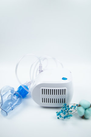 Vertical photo inhaler for home use lying on a white background next to blue flowers. The concept of treating respiratory diseases, lung diseases, prevention and self-care. High quality photoの写真素材