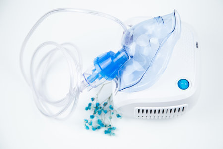 Top view of the breathing blue mask of the inhaler lies on the device and next to the flowers on a white background. The concept of treating respiratory diseases, lung diseases, prevention and self-care. High quality photoの写真素材