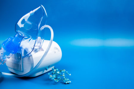 Close-up side view of a blue mask and a camera on a blue background with space for text. The concept of treating respiratory diseases, lung diseases, prevention and self-care.の写真素材