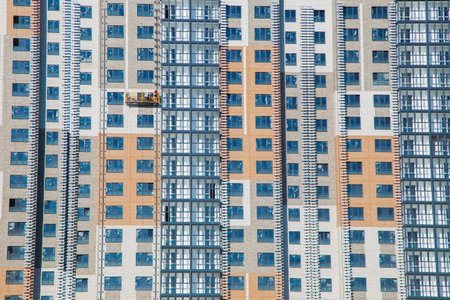 Workers on the scaffolding wash the windows of a high-rise building against a clear blue sky,...