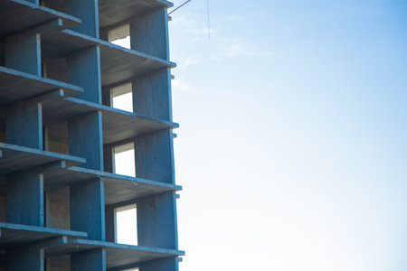 The construction site of a concrete building with visible empty window frames against a clear blue sky, highlighting the architectural process and the growth of the city with space for text against the sky. High quality photoの写真素材