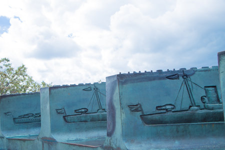 The relief sculpture depicts boats on the water, highlighting artistic details and textures, surrounded by a natural landscape with clouds and trees enhancing the atmosphere. High quality photoの写真素材