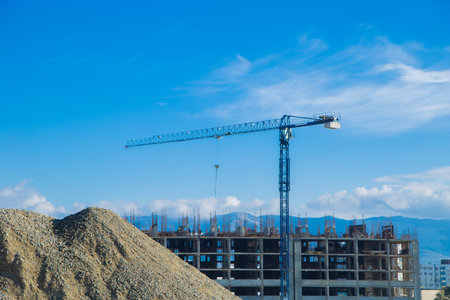 The construction site with a tower crane and a pile of gravel next to the building under construction emphasizes the dynamic nature of urban development and engineering. The concept of an apartment complex, a multi-storey building, the territory of the construction site. High quality photoの写真素材
