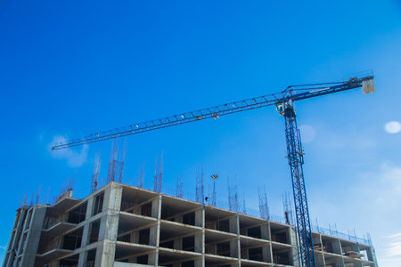 A tall construction crane on a construction site under a bright blue sky, illustrating the citys continued development and architectural progress in a dynamic environment. The concept of building a site, erecting houses, a multi-storey building. High quality photoの写真素材