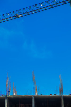 A construction site with a crane towering over a building under construction shows steel reinforcement against a clear blue sky, highlighting industrial progress and development. Concept of construction, monolithic structures, construction site. High quality photoの写真素材