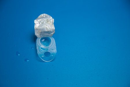 Close-up of a disposable container with a contact lens surrounded by water droplets on a blue...