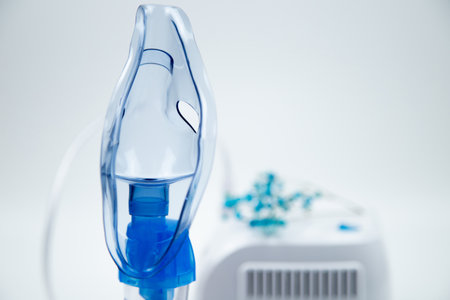 Close-up of a blue inhalation mask on the side, next to a white device out of focus with blue...