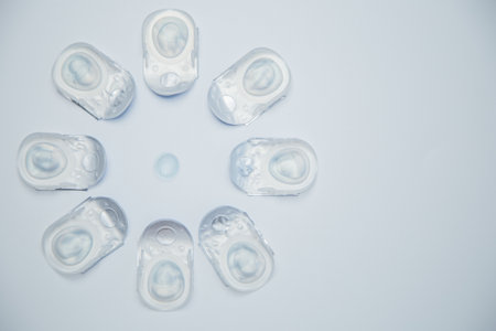 Creative flower layout of one-day contact lenses in disposable protective packaging, in the center is a transparent contact lens on a white background. The concept of ophthalmology, vision correction, eye care. High quality photoの写真素材