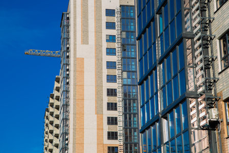 Modern residential buildings are being built with cranes in the foreground against a bright blue...