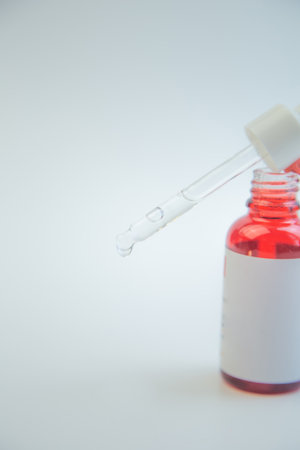 Dropper filled with vibrant red liquid hovers above a glass bottle, emphasizing skincare product design with a clean background, perfect for marketing and brandingの写真素材