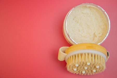 Body scrub in silver container paired with a natural bristle brush on a bright pink backdrop, emphasizing indulgent self-care and beauty routinesの写真素材