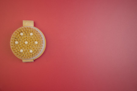 Exfoliating body brush with soft bristles, positioned on bright red surface, highlighting beauty tools for skincare and personal grooming, ideal for self-care routinesの写真素材
