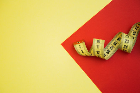 Measuring tape placed on a bright yellow and red geometric background, highlighting vivid colors and...