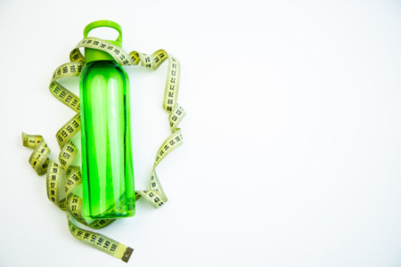 A vibrant green water bottle is artistically placed with measuring tape, representing health and fitness concepts, with clear copy space for creative useの写真素材