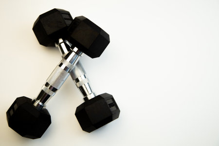 Crossed black hex dumbbells on a pristine white background, highlighting fitness equipment for strength training, perfect for gym enthusiasts and health-conscious individuals seeking motivationの写真素材