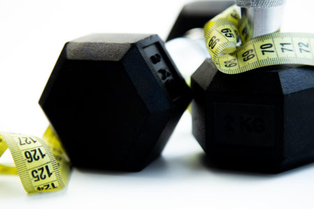 Two black hexagonal dumbbells placed next to a yellow measuring tape, representing fitness and health, perfect for workout themes and promoting an active lifestyle with copy spaceの写真素材