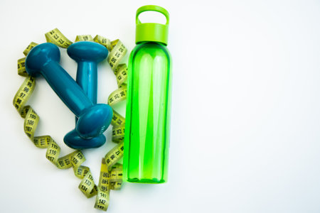 Vibrant dumbbells and a green water bottle are creatively arranged in a heart shape with measuring tape, representing a healthy lifestyle and fitness motivationの写真素材