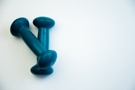 Teal dumbbells are placed on a smooth white surface, emphasizing fitness equipment for workouts, ideal for promoting a healthy lifestyle and exercise motivationの写真素材