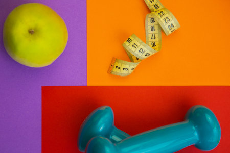 Vibrant arrangement of a green apple, measuring tape, and blue dumbbell on colorful geometric...