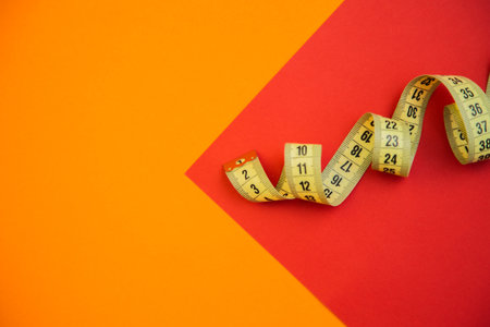 Curled yellow measuring tape rests on a bright orange and red geometric background, highlighting...