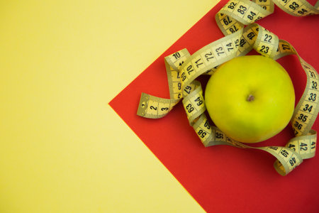 Fresh green apple on bright red and yellow backdrop, wrapped with measuring tape, representing...