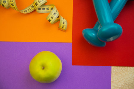 Fresh green apple on colorful surface with measuring tape and dumbbells, representing healthy living, fitness goals, and wellness choices in a vibrant settingの写真素材