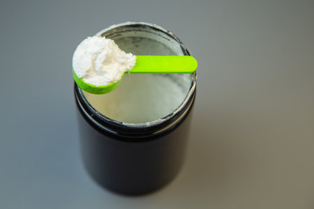 Close-up of a black container with a green scoop filled with white powder, highlighting nutritional content and health benefits for fitness and wellness enthusiastsの写真素材